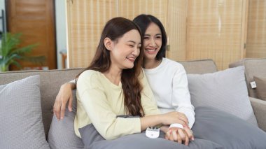 Livingroom 'da birlikte gülen LGBTQIA lezbiyen çifti. Asyalı LGBTQIA lezbiyen çift kanepede otururken birlikte mutlu bir şekilde güldüler. Homoseksüel-LGBTQ kavramı..