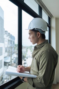 Mühendis ya da mimar elinde bir kalem tutuyor. İnşaat alanının planı üzerinde çalışıyor..