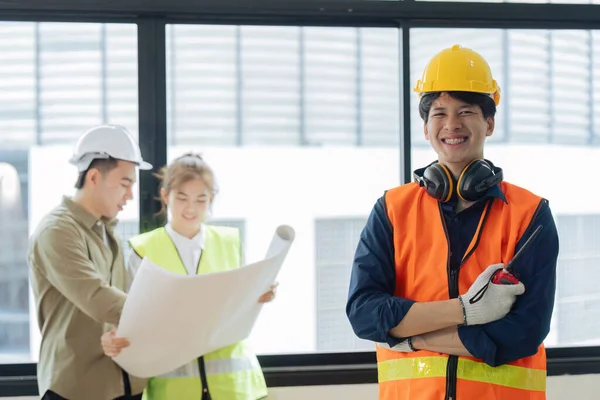 Portrait of civil engineer with hard hat holding radio walkie talkie while civil engineer planning in background.