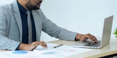 Şirketlerin mali belgelerindeki rakamları hesaplamak için hesap makinesi kullanan bir işadamı, şirketin nasıl büyüyeceğini planlamak için tarihsel finansal verileri analiz ediyor. Mali konsept..