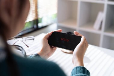 CHIANG MAI, THAILAND - 01 Eylül 2023: Kadınlar akşamları ekranlarında kırmızı Netflix marka logo ile iPhone 14 Pro tutarlar. Netflix küresel bir video yayınlama hizmetidir..