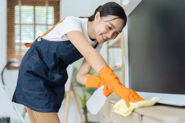 Młoda Kobieta Sprzątanie Pomocą Sprayu Wycieranie Szafki Telewizor Mikrofibry Tkaniny — Zdjęcie stockowe