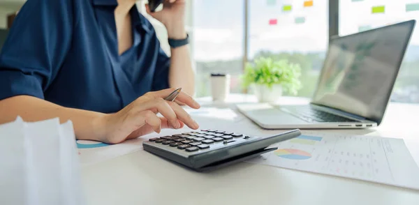 Bir şirketin mali belgelerindeki rakamları hesaplamak için hesap makinesi kullanan bir iş kadını, şirketin nasıl büyüyeceğini planlamak için tarihsel finansal verileri analiz ediyor. Mali konsept..