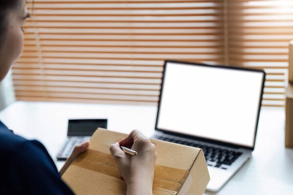 Young woman online business owner is preparing a parcel box to prepare the package for delivery to the customer.