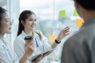İş adamları ofiste buluşup, fikirlerini paylaşmak için not tutuyorlar. Beyin fırtınası konsepti. Cam duvara yapışkan bir not..