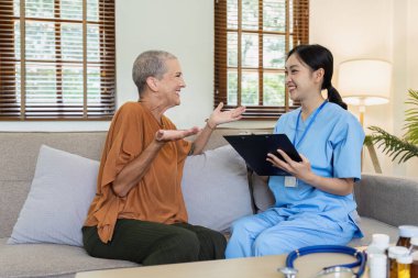 Hemşire panosu ve ev sigortası olan yaşlı bir kadın ve kanepede gülümseyen bir gülümseme..