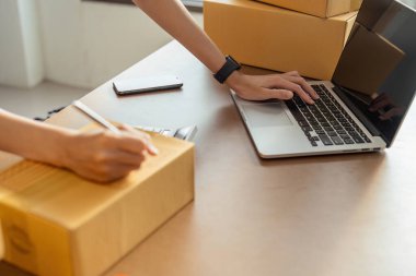 Genç kadın çevrimiçi işyeri sahibi paketin teslimatı için dizüstü bilgisayar kullanıyor..