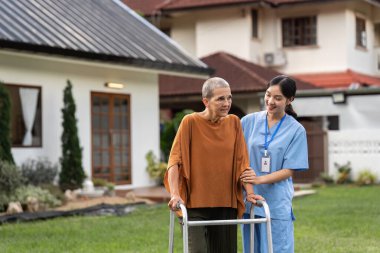 Hemşire ya da bakıcı yaşlılara bahçede yürümeleri için yardım ediyor..