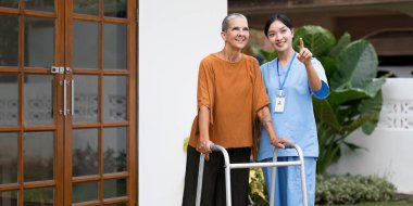 Hemşire ya da bakıcı yaşlılara bahçede yürümeleri için yardım ediyor..