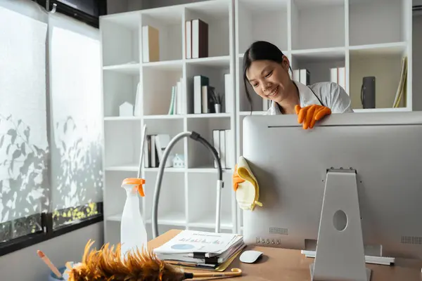 Woman maid cleaning and wiping the computer with microfiber cloth in office.