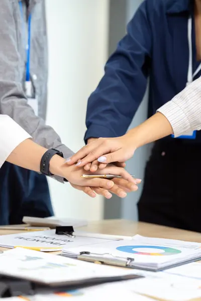 Businesspeople stack their hand on top of each other, indicating success after work meeting in conference room.