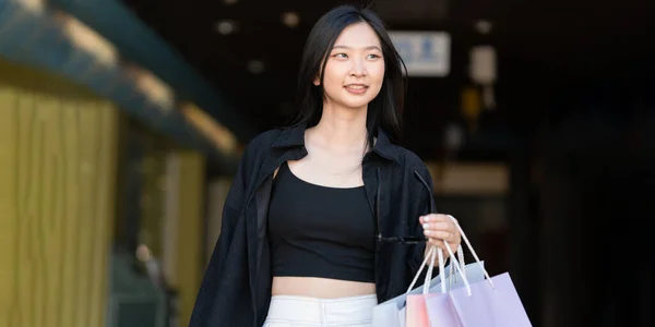 Young asian woman in shopping. Fashion woman in black with shopping bag walking out store after shopping. Black friday.