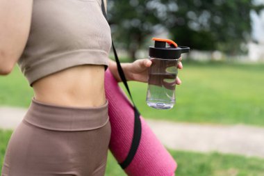 Parkta koştuktan sonra elinde su şişesi olan fitness kadını..
