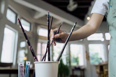 Kadın sanatçı, hobi atölyesi sırasında resim yapmak için renk paleti ve boya fırçasına sahip.