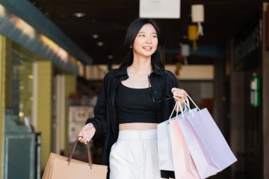 Alışveriş yapan Asyalı genç bir kadın. Alışveriş yaptıktan sonra alışveriş çantası taşıyan siyah elbiseli bir kadın. Kara Cuma.