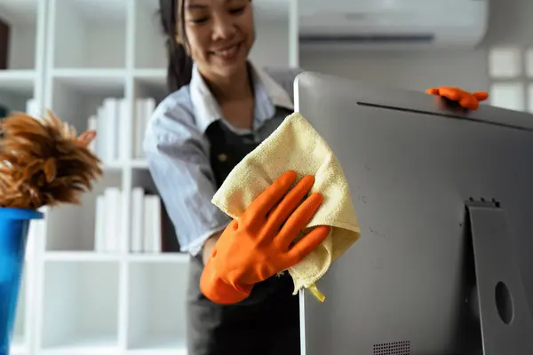 Woman maid cleaning and wiping the computer with microfiber cloth in office.