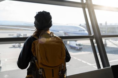 Gezgin kadın plan ve sırt çantası havaalanı cam penceresinde uçak uçuşuna bakın..