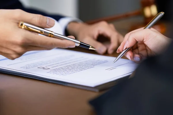 Avukatın elleri iş adamlarının kontrat imzalaması için kağıtları işaret ediyor. Avukat ve hukuk danışmanı olgun müşterilerin belgeleri doldurmasına yardım ediyor.