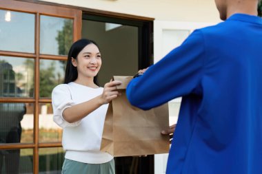 Asyalı genç teslimatçı kadın müşteriye paket teslim ediyor..