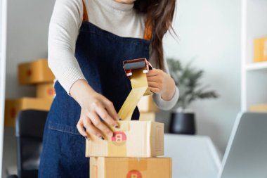 Genç girişimci bir kutuyu bantla mühürlüyor. Nakliyeye, paketlemeye, çevrimiçi satışa, e-ticaret konseptine hazırlık.