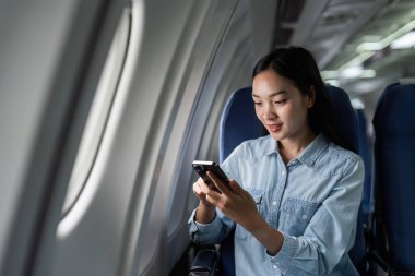 Uçakta cep telefonu kullanan Asyalı bir kadın var..