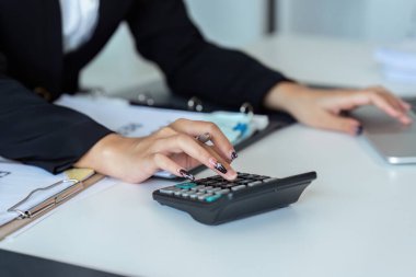 Bir şirketin mali belgelerindeki rakamları hesaplamak için hesap makinesi kullanan bir iş kadını, şirketin nasıl büyüyeceğini planlamak için tarihsel finansal verileri analiz ediyor. Mali konsept.