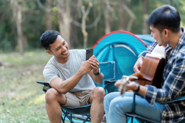 LGBTQIA Gay çifti tatil için ormanda kamp kuruyor ve birlikte gitarda dinleniyorlar..
