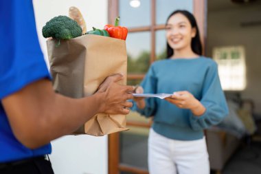 Asyalı genç teslimatçı kadın müşteriye paket teslim ediyor..