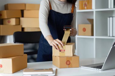 Genç girişimci bir kutuyu bantla mühürlüyor. Nakliyeye, paketlemeye, çevrimiçi satışa, e-ticaret konseptine hazırlık.