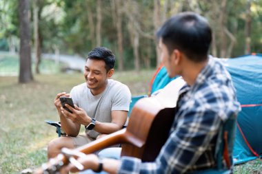 LGBTQIA Gay çifti tatil için ormanda kamp kuruyor ve birlikte gitarda dinleniyorlar..