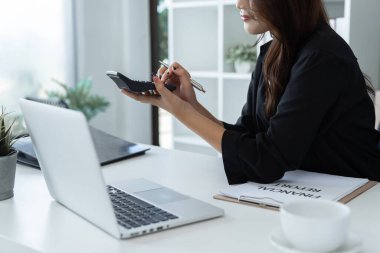 Bir şirketin mali belgelerindeki rakamları hesaplamak için hesap makinesi kullanan bir iş kadını, şirketin nasıl büyüyeceğini planlamak için tarihsel finansal verileri analiz ediyor. Mali konsept.