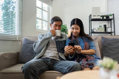 Emekli yaşlı çift kanepede oturur çay içer ve cep telefonlarını birlikte kullanır ve evlerinde dinlenirler. Kıdemli Etkinlik Konsepti.