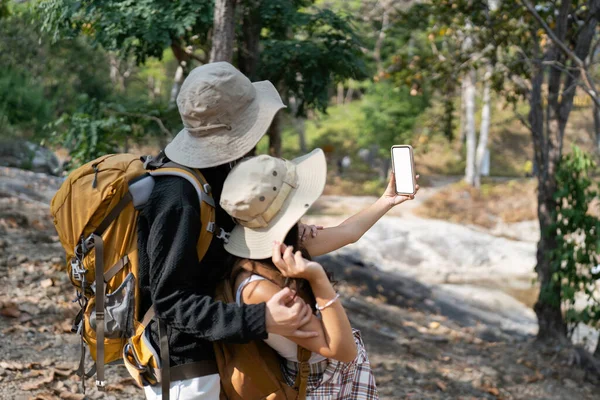 Happy LGBT Lesbian couple selfie with mobile while Hiking with Backpacks in forest Trail. LGBT Lesbian Couple Hikers with backpacks walks in mountains in vacation.