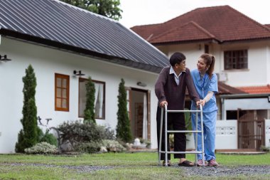 Hemşire ya da bakıcı yaşlılara bahçede yürürken yardım ediyor..