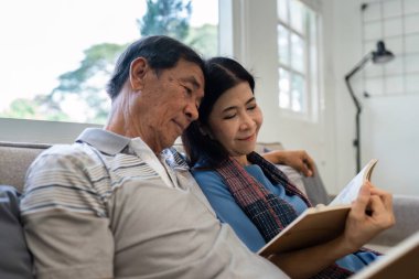Emekli yaşlı çift evlerindeki kanepede oturup rahatlama kitabı okuyor. Kıdemli Etkinlik Konsepti.