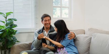 Emekli yaşlı çift kanepede oturur çay içer ve cep telefonlarını birlikte kullanır ve evlerinde dinlenirler. Kıdemli Etkinlik Konsepti.