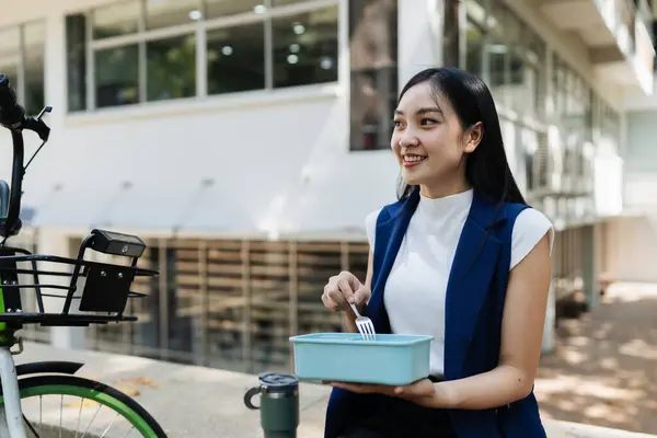 Asian young businesswoman bike to work for eco friendly green energy and eat lunch using box lunch prepared from home. while commuting in city. Eco friendly.