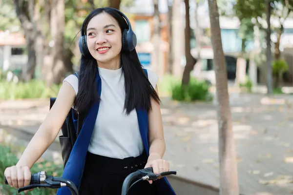 Asian young businesswoman bike to work for eco friendly green energy and listen music with headphone while commuting in city. Eco friendly.