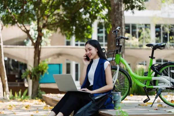 Young businesswoman sitting on stair in city park and using laptop for work hybrid. Bike to work eco friendly alternative vehicle green energy.