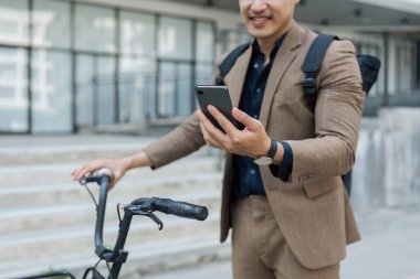 Asyalı genç işadamı şehirde iş seyahatinde akıllı telefon kullanır. Çevre dostu.