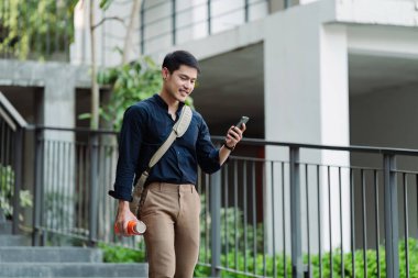 Gülümseyen Asyalı işadamı yeniden kullanılabilir çevre dostu ekolojik fincanı elinde tutuyor ve eve dönerken cep telefonu kullanıyor..