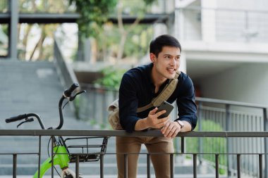Asyalı genç işadamı şehirde iş seyahatinde akıllı telefon kullanır. Çevre dostu.