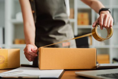 Genç girişimci bir kutuyu bantla mühürlüyor. Nakliyeye, paketlemeye, çevrimiçi satışa, e-ticaret konseptine hazırlık.