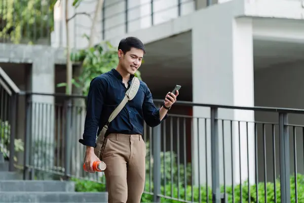 Smiling asian businessman hold reusable eco-friendly ecological cup and using mobile while on the way home at park.