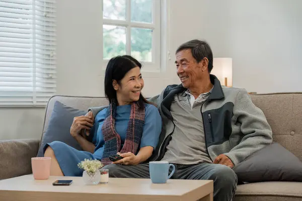 Older couples sit and chat and head over each other relaxed and happy on sofa at home on weekday in comfortable.