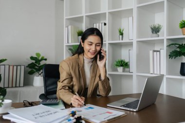 İş kadını analizi, dizüstü bilgisayarla çalışırken cep telefonuyla yeni projeyi tartışıyor.