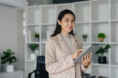 Dijital tablet kullanan kendine güvenen iş kadını masanın önünde duruyor..