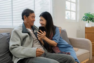 Emekli yaşlı çift kanepede oturur çay içer ve cep telefonlarını birlikte kullanır ve evlerinde dinlenirler. Kıdemli Etkinlik Konsepti.