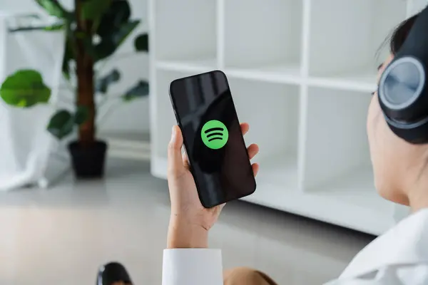CHIANG MAI, THAILAND - 20 Mart 2024: Bir kadın ekranda Spotify uygulamalı Apple iPhone 'u tutuyor ve kulaklık takıyor.