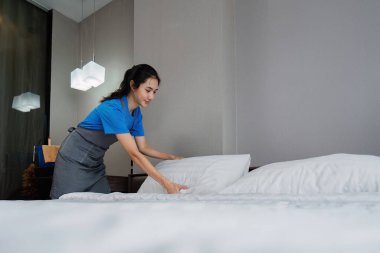 Temizlikçi kadın, evde temiz yatak odası. Temizlikçi kendini mutlu hisseder ve yatağı temiz gösterir. ev işleri ve temizlik servisi.